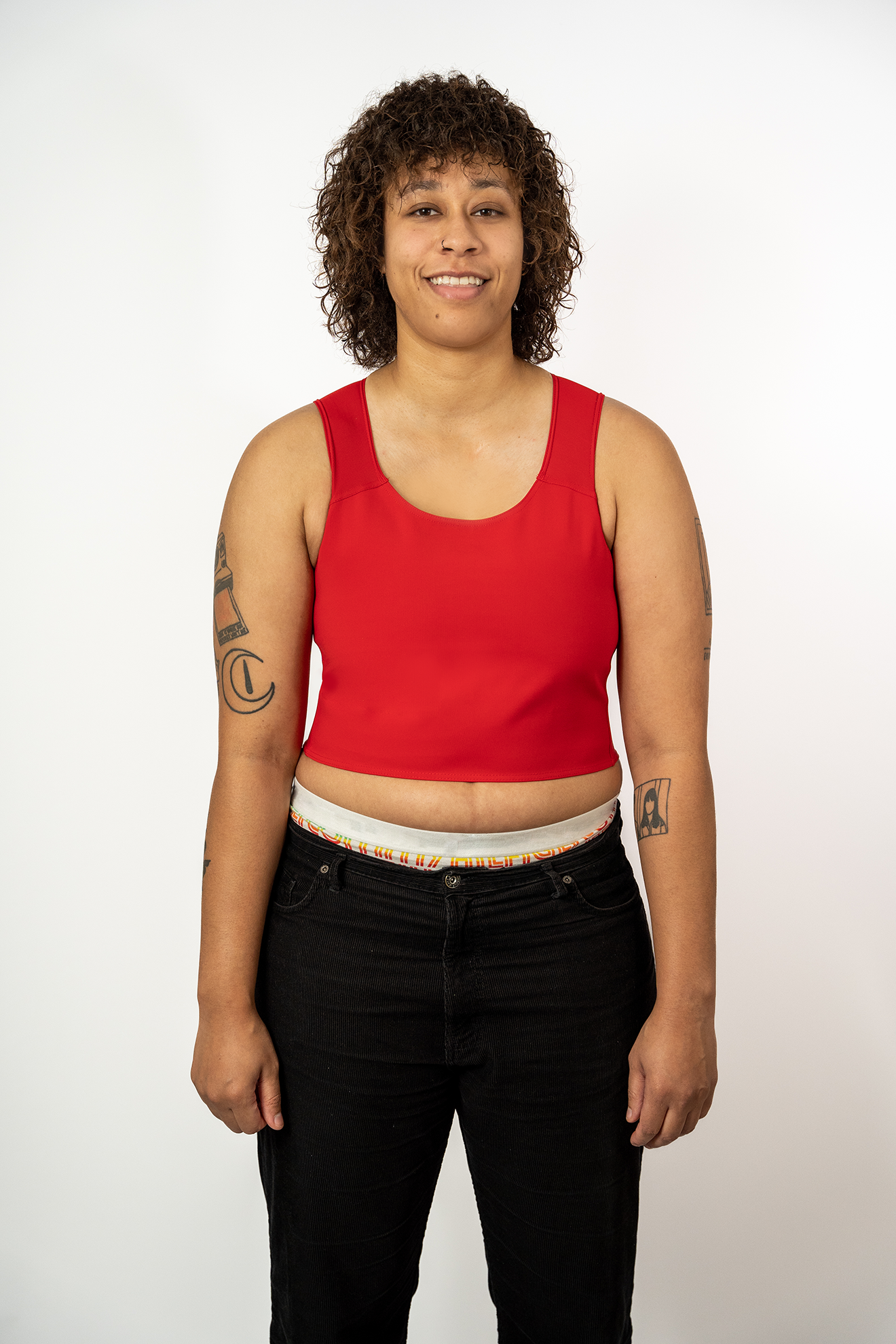 Person wearing a Berry coloured short chest binder and black jeans against a white background