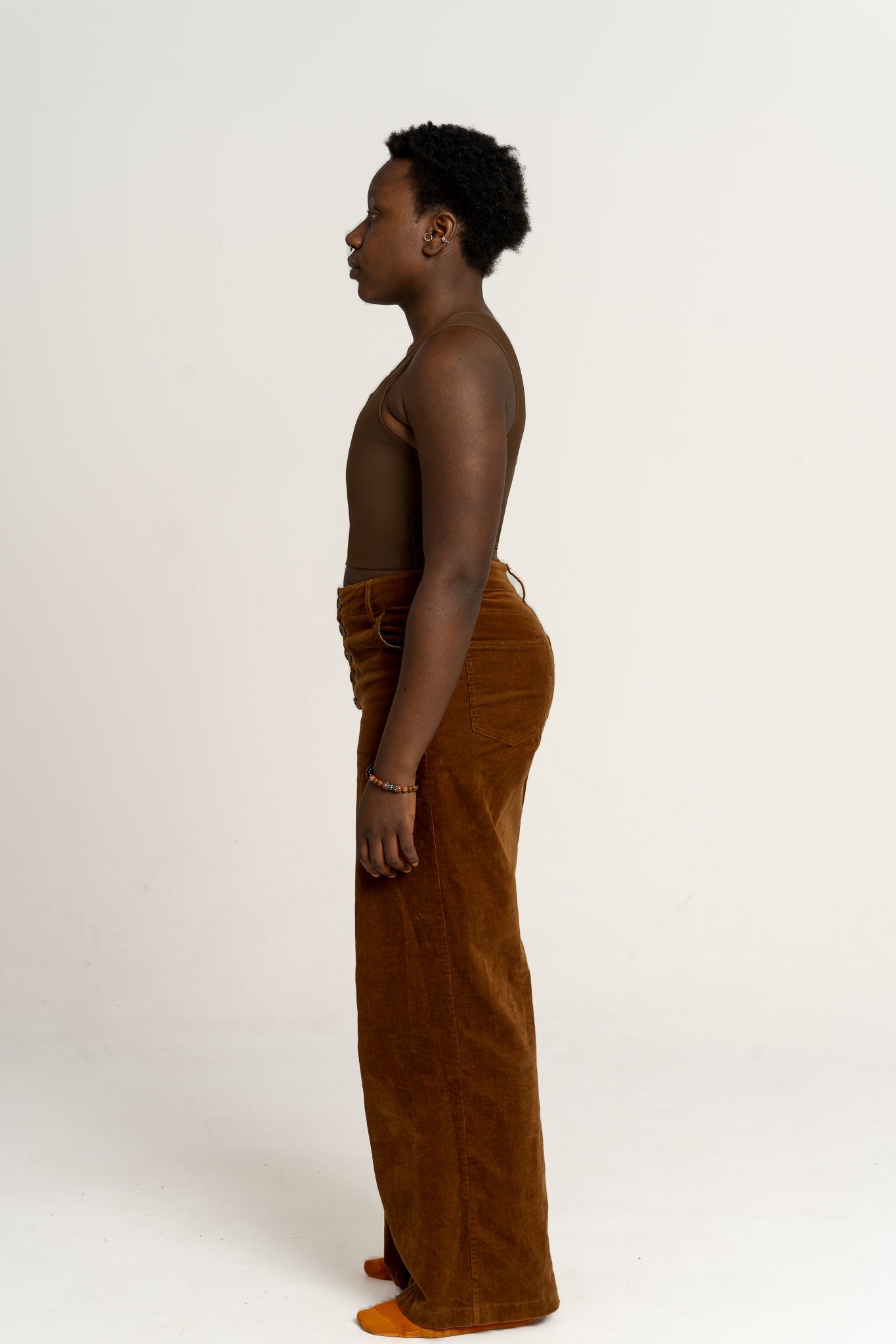 Person wearing a dark long chest binder and dark orange pants against a beige background.