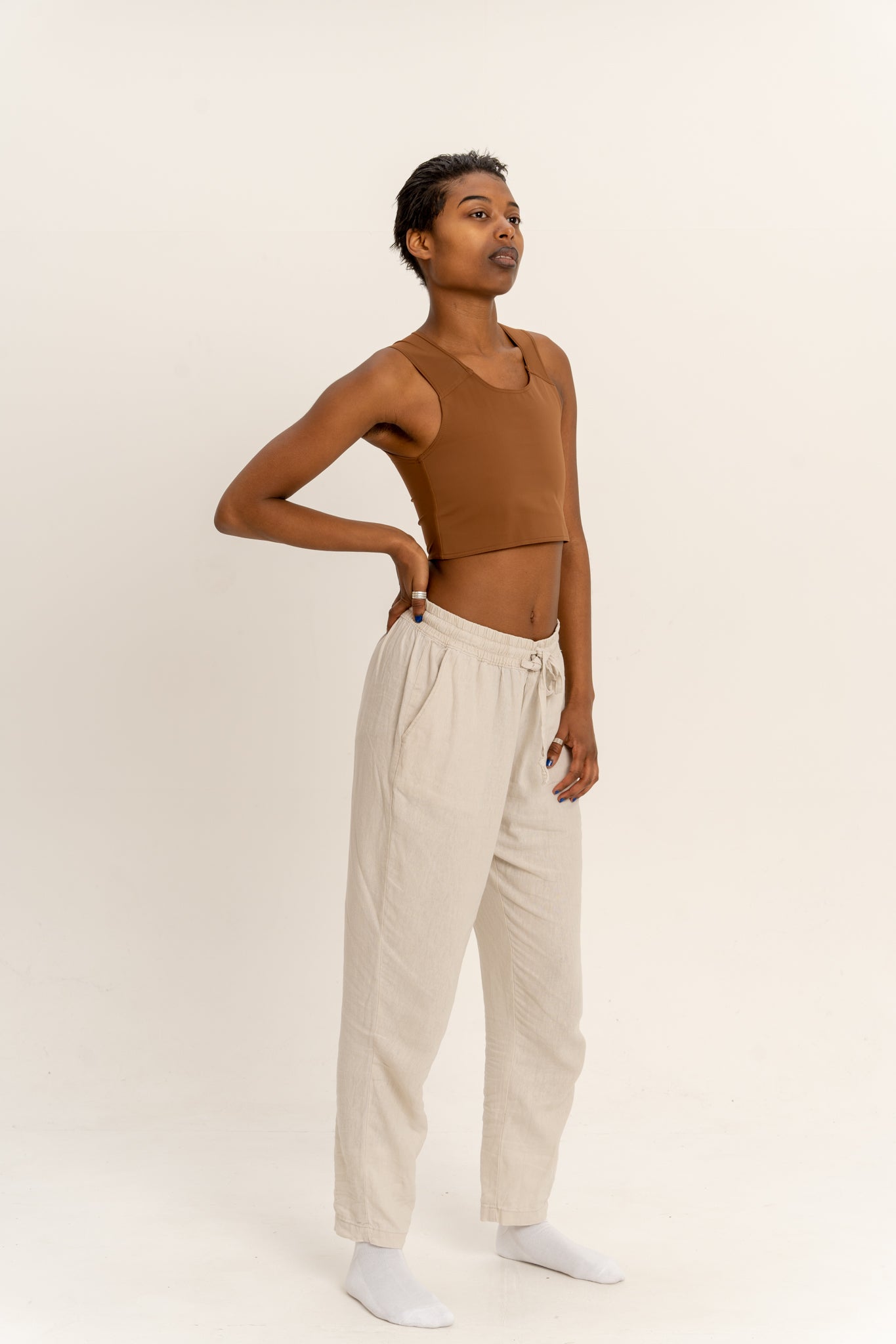 Person wearing a deep short chest binder and beige pants against a white background