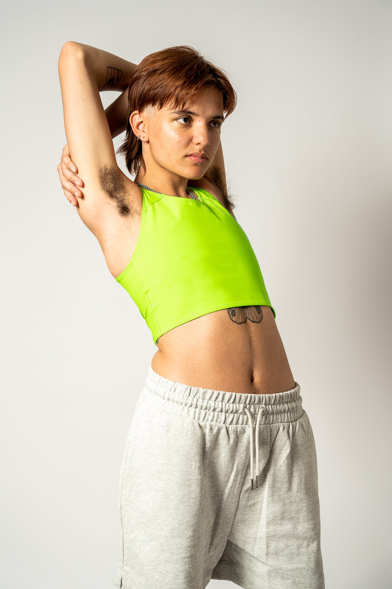 Person wearing an acid green coloured short chest binder and grey joggers against a white background