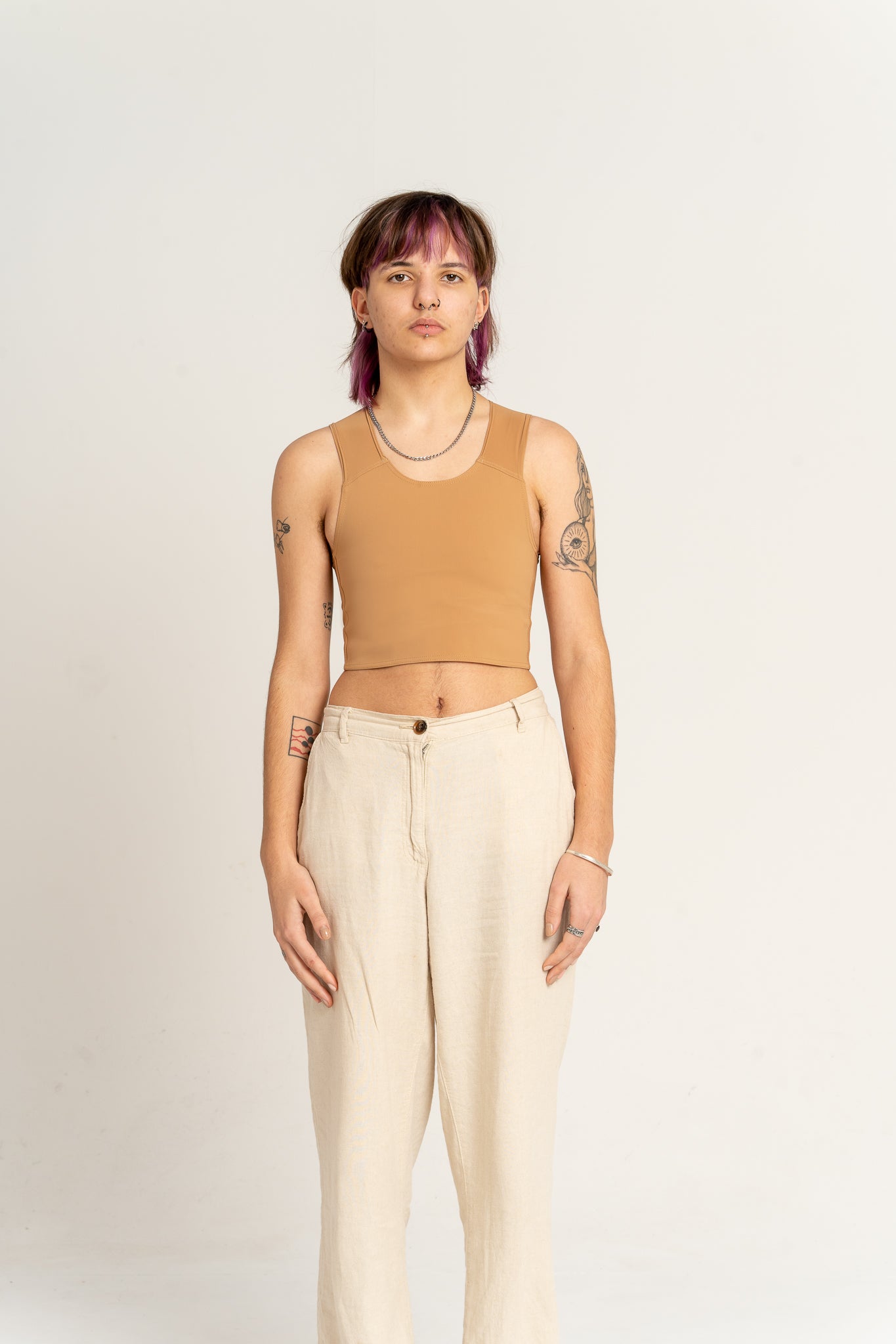 Person wearing a medium toned long chest binder and beige pants against a beige background
