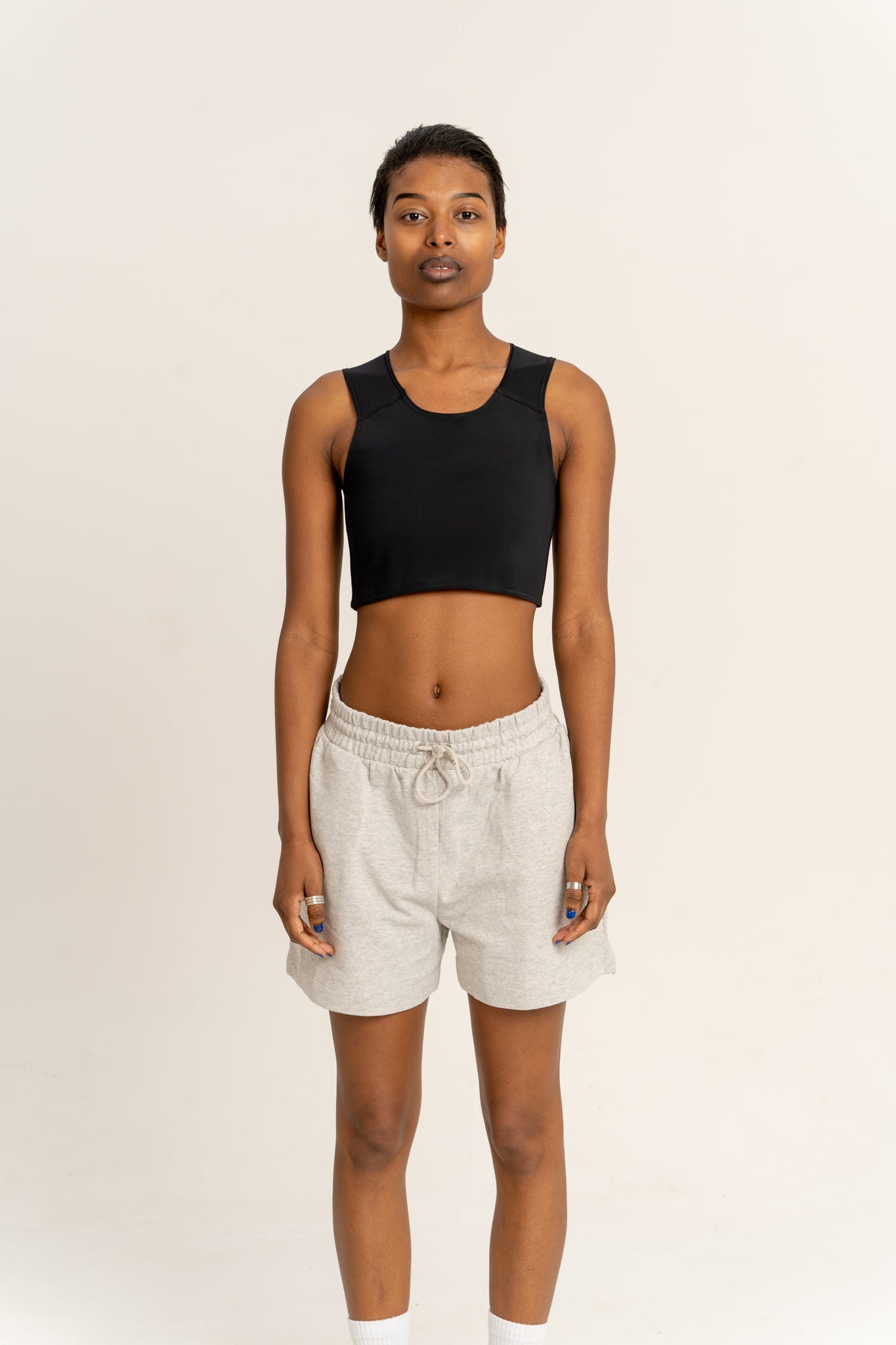 Person wearing a black chest binder and light-colored shorts on a plain background