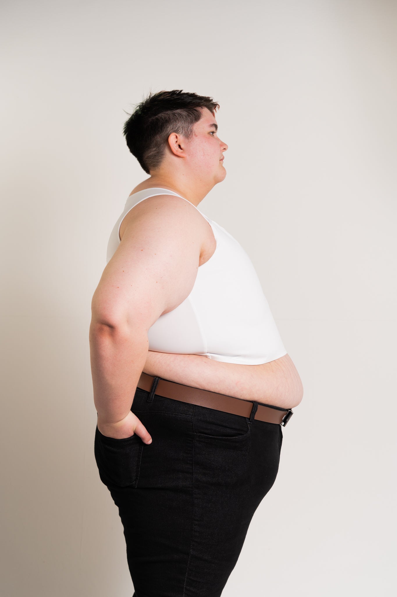Person wearing a white chest binder and black pants against a plain background