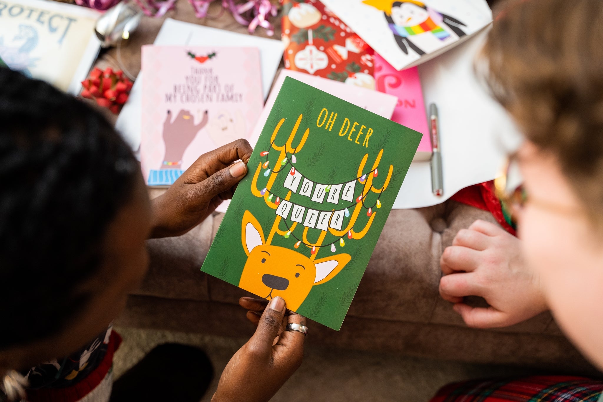 Two people holding a green card reading 'Oh deer you're queer' with a deer illustration.