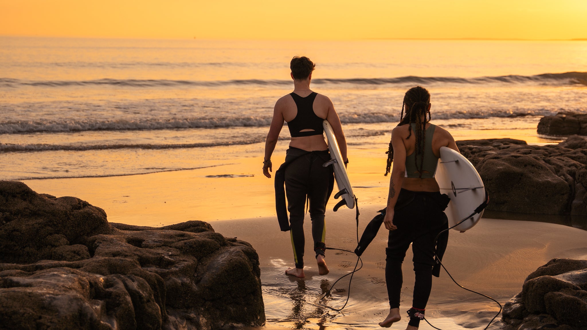 Two people surfing at sunset wearing chest binders