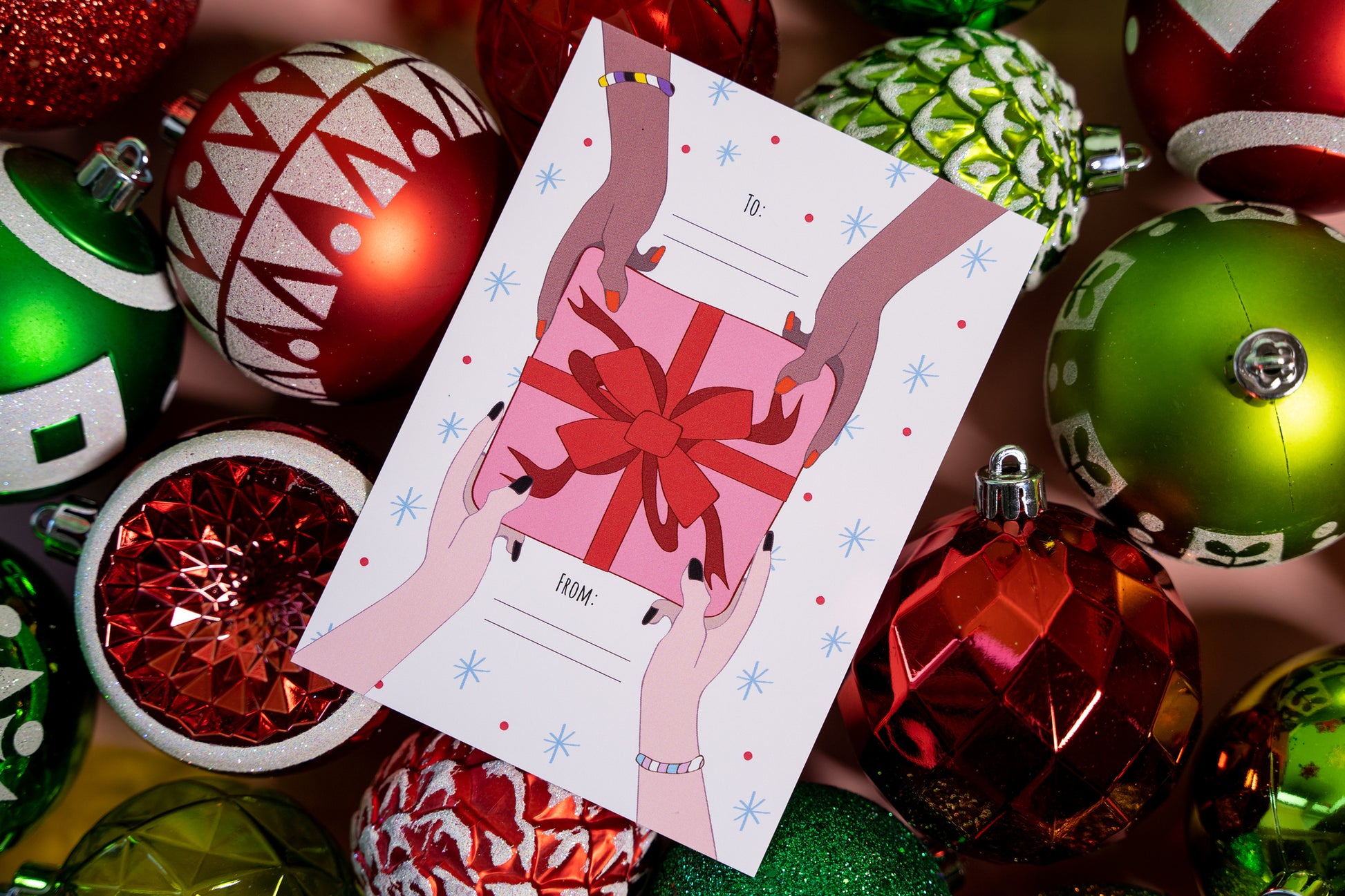 Card with hands holding a gift card surrounded by colorful Christmas ornaments.