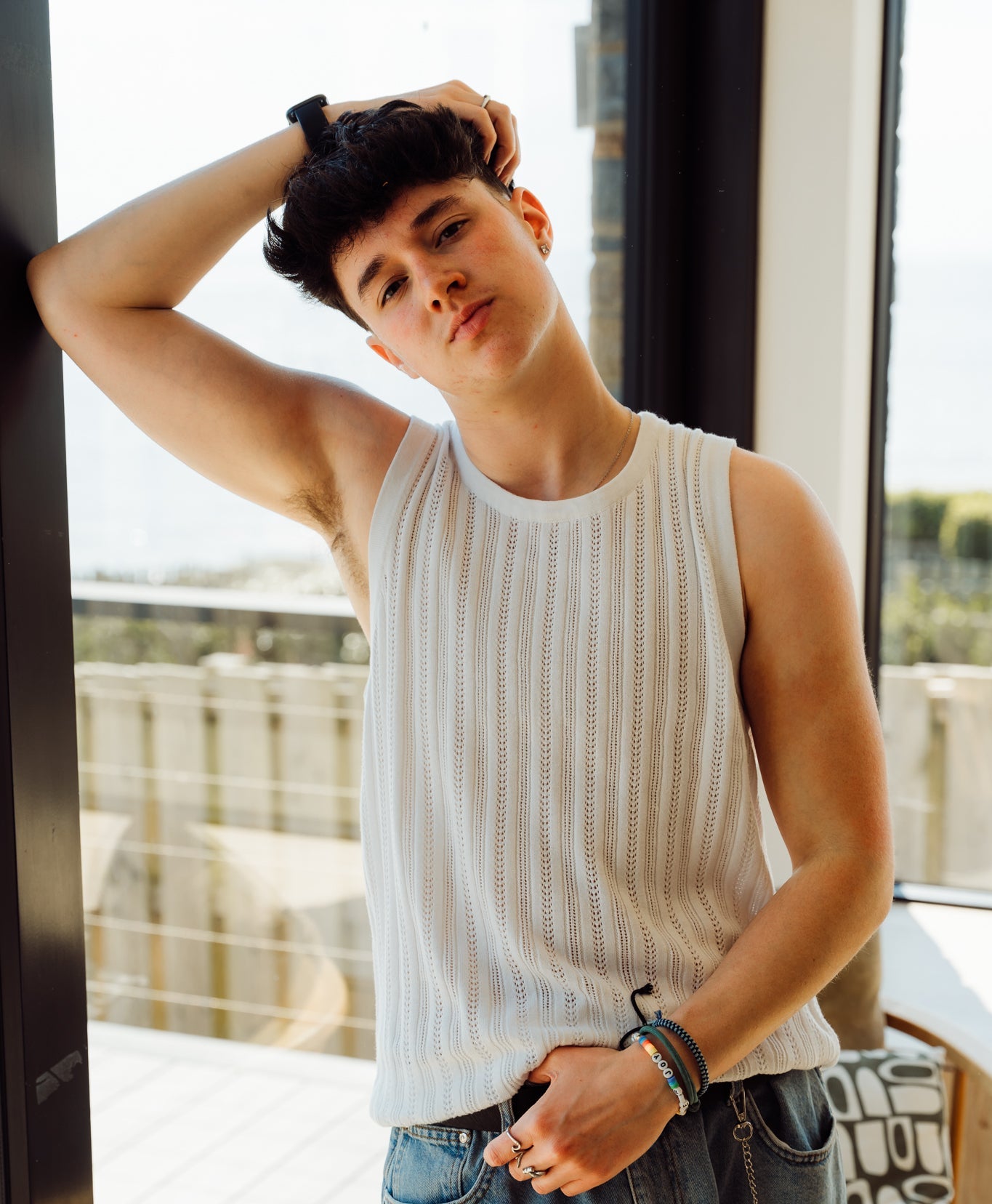 A trans man wearing a white vest top over a chest binder that is not visible.