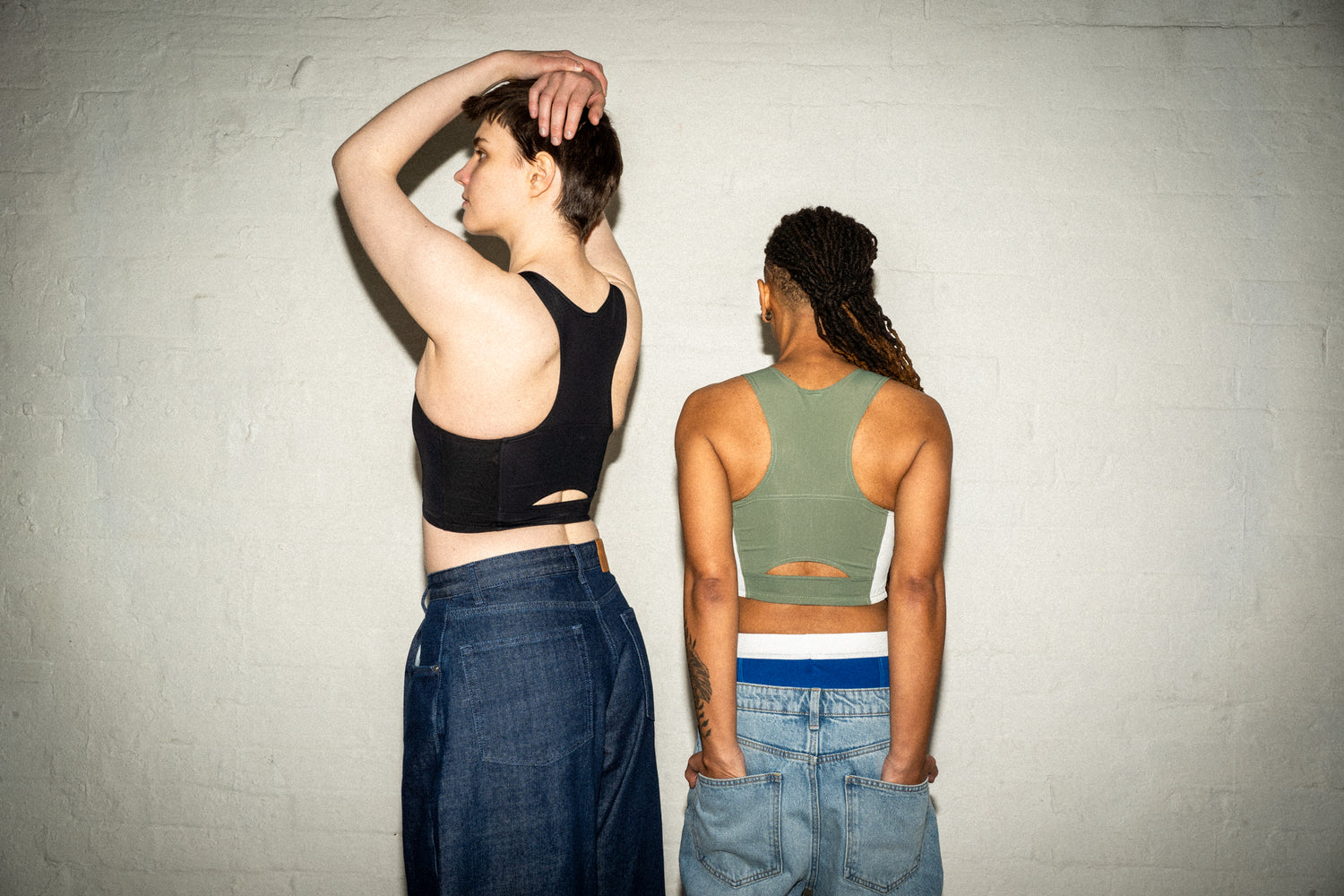 Two transgender people wearing chest binders looking away from the camera 
