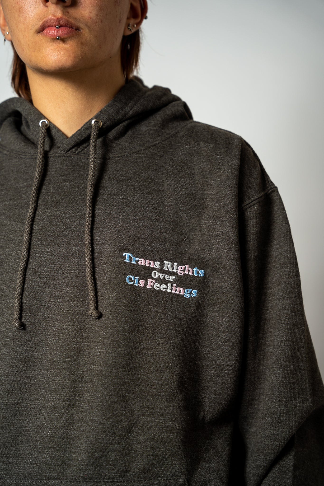 Person wearing a dark gray hoodie with 'Trans Rights Over Cis Feelings' text.