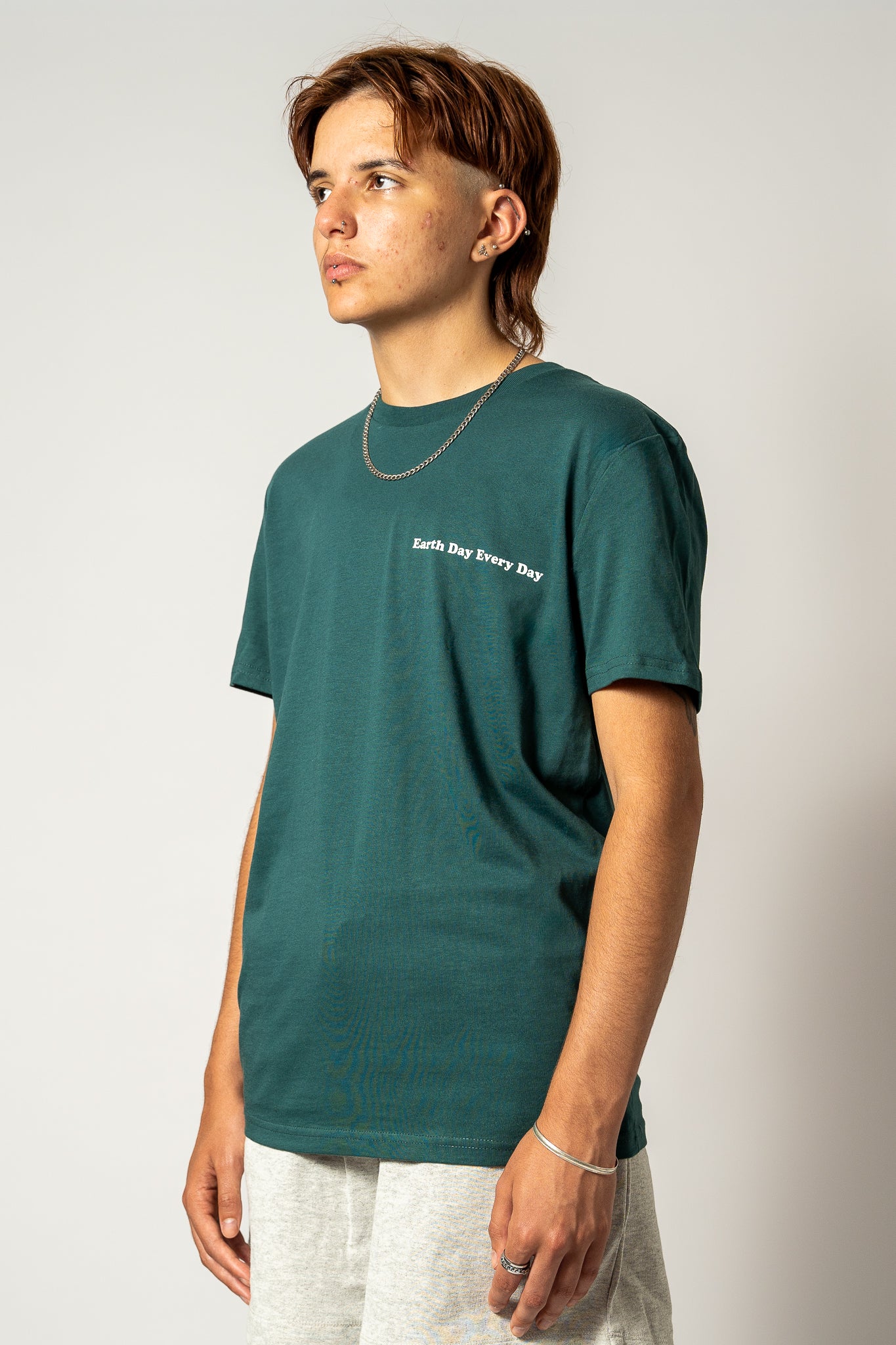 Person wearing a green "Earth Day Every Day" t-shirt with text on a plain background.